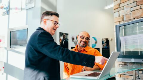Zwei Menschen stehen nebeneinander und schauen in den Laptop.